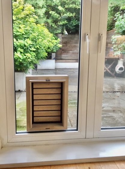 Trappes pour Chien | Bouncer (Large) porte pour chien en bois installé dans la fenêtre d'une porte vitrée d'une terrasse | © Tomsgates